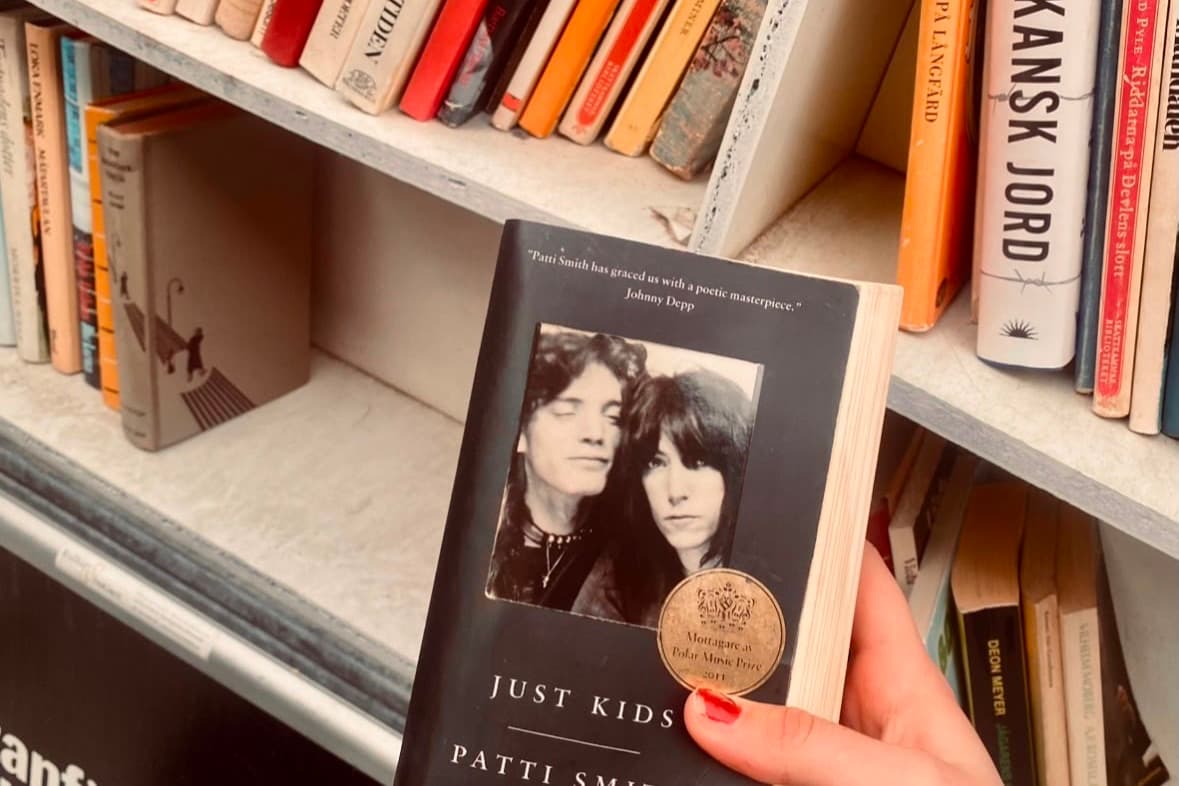 A hand lifting a well-read paperback from a crowded second-hand bookshop shelf.